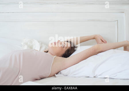 Donna sdraiata sulla schiena nel letto stretching Foto Stock