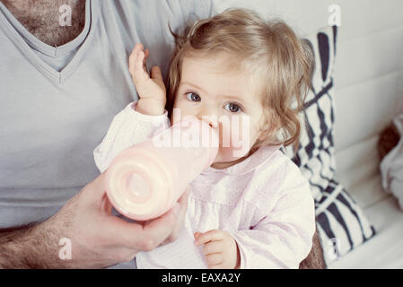 Baby ragazza seduta sul padre, giro di bere dalla bottiglia, ritagliato Foto Stock