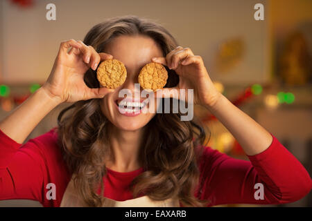 Ritratto di giovane felice casalinga tenendo i cookie nella parte anteriore degli occhi Foto Stock