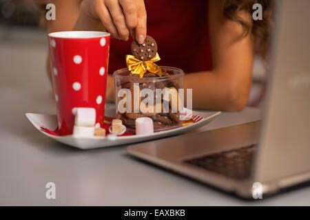 Primo piano su buon giovane casalinga con spuntini di natale utilizzando laptop in cucina Foto Stock