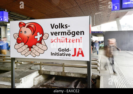 Zurigo, Svizzera. Xxi Nov, 2014. Persone alla stazione principale di Zurigo sono passando dietro un referendum campagna di manifesti della Swiss 'Gold iniziativa' referendum che si terrà il Nov 30, 2014. Con una settimana a visitare la campagna referendaria del Swiss 'Gold iniziativa' sta andando a piena potenza in tutta la Svizzera. Il controverso referendum è volto a forzare la Banca Nazionale Svizzera per tenere almeno il 20% di tutti i beni in oro fisico. Credito: Erik Tham/Alamy Live News Foto Stock