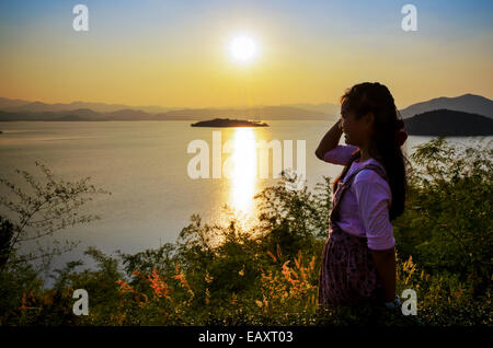 Felice giovane donna in piedi sulla collina a guardare il tramonto sul lago in Kaeng Kra Chan National Park, Phetchaburi Provincia, Foto Stock