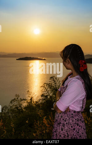 Felice giovane donna in piedi sulla collina a guardare il tramonto sul lago in Kaeng Kra Chan National Park, Phetchaburi Provincia, Foto Stock