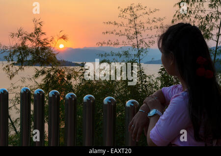 Felice giovane donna in piedi sulla collina a guardare il tramonto sul lago in Kaeng Kra Chan National Park, Phetchaburi Provincia, Foto Stock