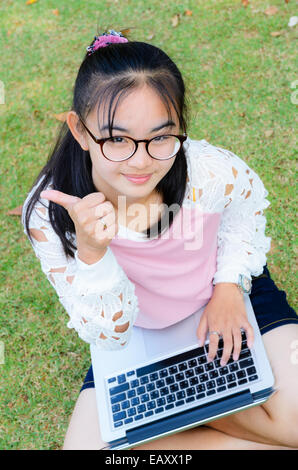 Bella ragazza è felice con un computer portatile sul prato in posizione di parcheggio Foto Stock