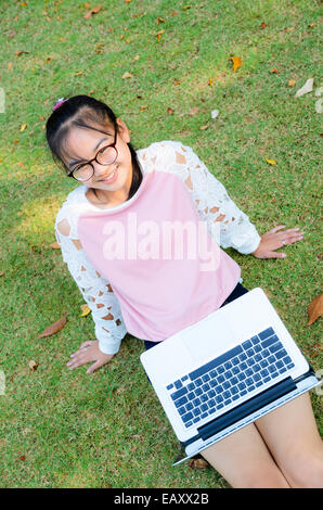 Ragazza carina è felice con il notebook su erba nel parco Foto Stock