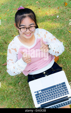 Ragazza carina è felice con il notebook su erba nel parco Foto Stock