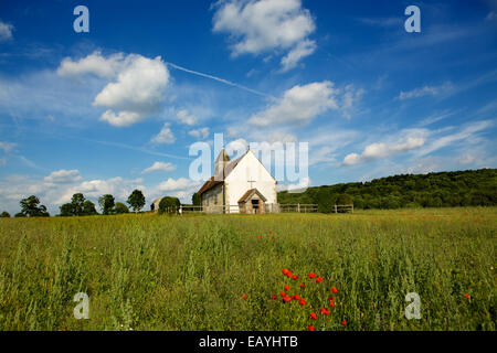 Chiesa sulla collina. St Hubert è una piccola chiesa medievale in piedi da solo in un prato selvatico. Papaveri rossi in primo piano. Foto Stock