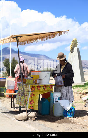 La donna in piedi alla bevanda stand tenendo un cucchiaio con un drink del quisa o kisa (disidratati peach) in Kasani, Bolivia Foto Stock