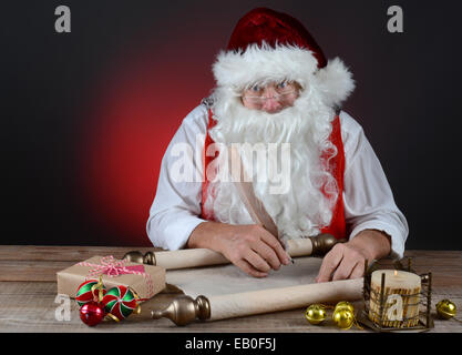 Babbo Natale nel controllo della sua naughty e bella lista in un rotolo di carta pergamena. Santa è seduto a una tavola in legno rustico. Horizonta Foto Stock