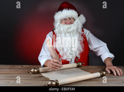 Santa Claus rendendo la sua naughty e bella lista in un rotolo di carta pergamena. Santa è seduto a una tavola in legno rustico. Posizione orizzontale Foto Stock