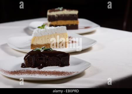 Selezione di dessert in un ristorante con una linea diagonale di tre diverse varietà di torta servito su piastre con una fetta o torta al cioccolato in primo piano. Foto Stock