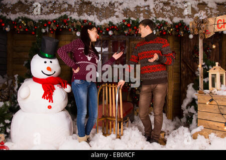 Coppia giovane in inverno abiti parlando all'interno della casa in legno, con attraenti decorazioni di Natale, accanto al grande neve al coperto Foto Stock