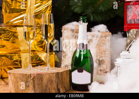 Festa di Natale ancora in vita con due flauti champagne su un moncone, bottiglia, registri, abete, lanterna e neve accanto a confezioni regalo w Foto Stock