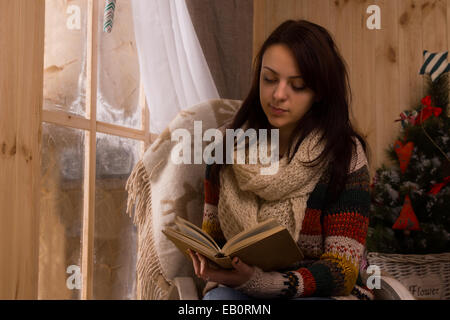 Attraente giovane donna seduta a fianco di lettura di un legno sabbiato vetro in inverno Foto Stock