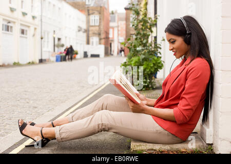 Giovane donna leggendo un libro e ascoltando la musica. Foto Stock