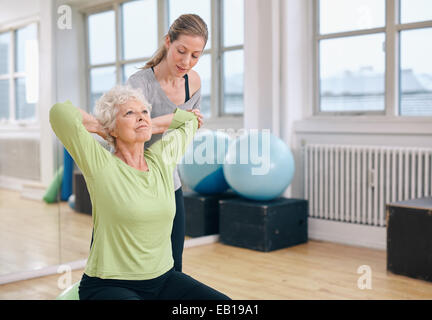 Le donne anziane facendo luce pilates allenamento per i muscoli della schiena con pullman assistenza. Trainer aiutando donna senior per gli esercizi in palestra. Foto Stock