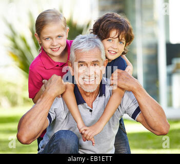 Felice il nonno con due bambini sorridenti in un giardino Foto Stock