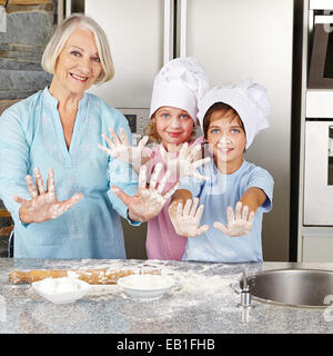 La famiglia felice con bambini che mostra le mani con la farina in cucina durante la cottura i cookie Foto Stock