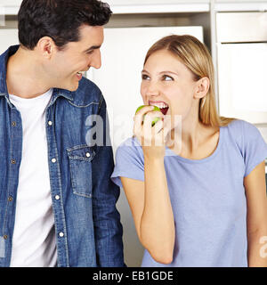 Donna felice di mangiare una mela verde vicino all uomo in una cucina Foto Stock