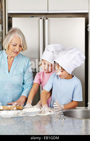 Due bambini la cottura biscotti di Natale con la loro nonna in cucina Foto Stock