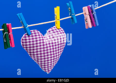 Cuore solo su stendibiancheria con clothespins, sfondo blu Foto Stock