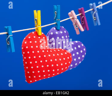 Due cuori appesi a un stendibiancheria con clothespins, focus sul rosso. Sfondo blu Foto Stock