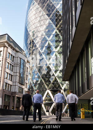 Un gruppo di quattro uomini di affari in giacca camminare insieme nella città di Londra. In fondo è 30 St Mary Axe, noto anche come Foto Stock