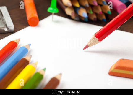 Matita rossa disegna sul foglio di carta bianco. Matite colorate, pastelli, eraser sul tavolo. Foto Stock