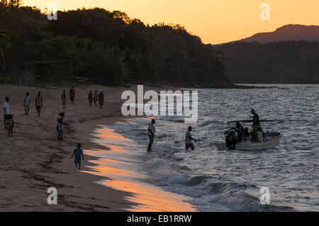 Enti locali cittadini malgasci camminando lungo una spiaggia al tramonto con barca Foto Stock