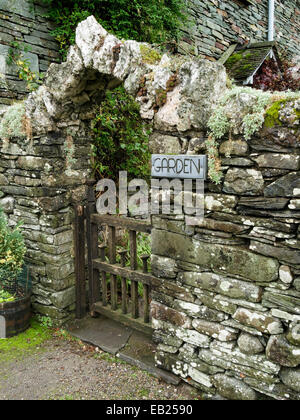 Vecchio muro di pietra a secco in ardesia con arco sopra cancello di legno nel giardino Foto Stock