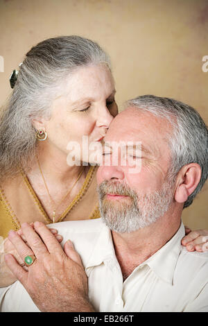 Bella donna senior dà il suo marito un affettuoso bacio sulla fronte. Aggiunta di vignette per effetto drammatico. Foto Stock