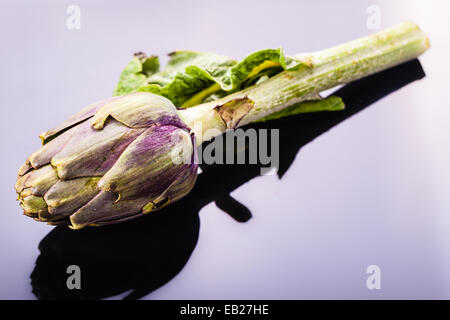 Un fresco verde carciofo su un elegante riflettente superficie nera Foto Stock