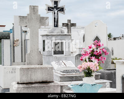 Tombe cristiane in marmo e pietra con croci e tomba offerta di fiori rosa brillante nel cimitero di Panteon de San Roman, Campeche, Messico. Foto Stock