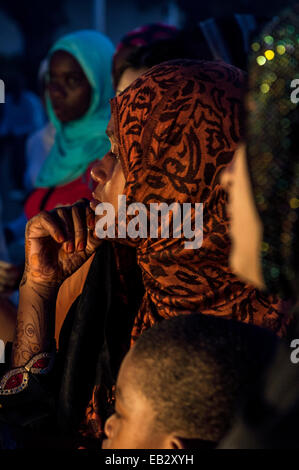 Una donna musulmana di Henna Tattoos attende di essere servita a una pressione di stallo di cibo in un affollato mercato notturno. Foto Stock