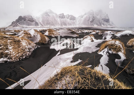Neve su nero dune di sabbia di fronte Vestrahorn montagna in inverno, nebbia, Stokksnes, Höfn, Islanda Foto Stock