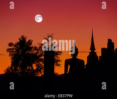 Buddha seduto al Wat Mahathat, silhouette al tramonto e luna piena, Sukhothai Historical Park, Sukhothai, Sukhothai Provincia Foto Stock