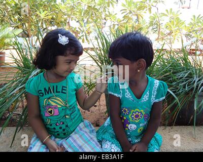 India, nello Stato del Tamil Nadu, Thoothukudi, Kalugumalai, due ragazze (2-3) seduto sul parapetto di aiuola in giardino, guardando ogni altro Foto Stock