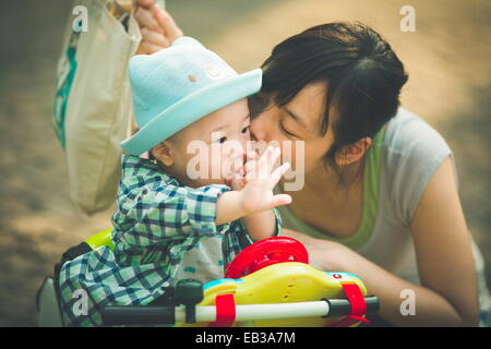 Madre baciando il figlio mentre si trova sul triciclo giocattolo Foto Stock