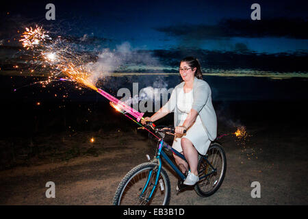 Donna che mantiene i fuochi d'artificio in bicicletta di notte Foto Stock