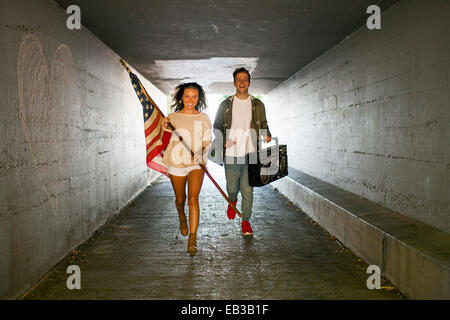 Caucasian matura portante bandiera americana e boom box nel tunnel Foto Stock