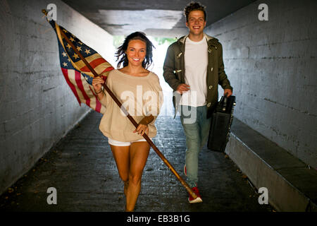 Caucasian matura portante bandiera americana e boom box nel tunnel Foto Stock