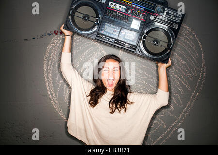 La donna caucasica holding boom box vicino a Chalk cuore sulla parete Foto Stock