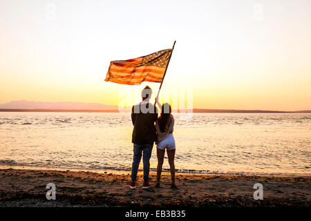 Caucasian giovane azienda bandiera americana sulla spiaggia Foto Stock