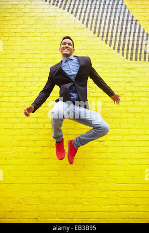 Uomo sorridente salti di gioia nei pressi di colore giallo brillante parete Foto Stock