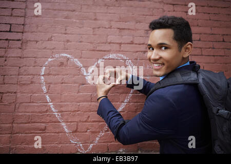 Uomo sorridente messa a forma di cuore con le mani dal cuore di chalk disegno sulla parete Foto Stock