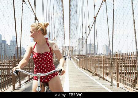 Donna sorridente Bicicletta Equitazione attraverso ponte urbano, New York New York, Stati Uniti Foto Stock