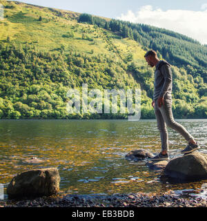 Uomo in piedi su rocce sulla riva del fiume, Scozia, Regno Unito Foto Stock