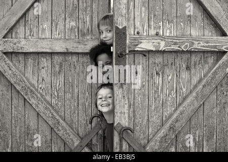 Tre bambini guardando fuori da dietro la porta Foto Stock