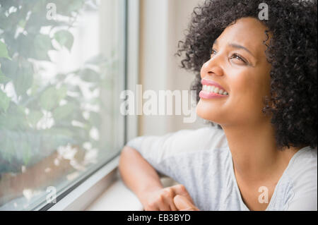 Donna sorridente a guardare fuori dalla finestra Foto Stock